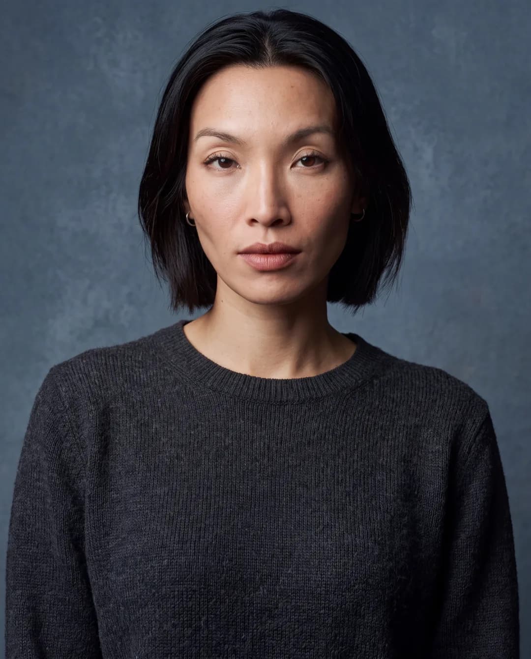 AI-generated First Look frame of Promptography cofounder Gift: a chest-up frontal studio portrait in the same charcoal sweater and blue-grey light